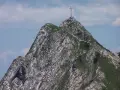Giewont z krzyżem na szczycie, skaliste zbocza, zielona trawa, błękitne niebo z chmurami.
