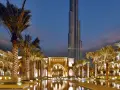 Wieczorny widok na Burdż Chalifa w Dubaju, otoczony palmami i basenami.