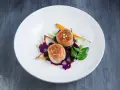 Eleganckie danie z dwóch medalionów mięsa zawiniętych w boczek, podane z purée, marchewką i kwiatami.