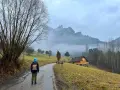 Osoba w niebieskiej czapce idzie drogą w Pieninach, w tle góry i drewniane chatki.