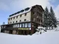 Hotel w Zieleńcu zimą, z widoczną wypożyczalnią nart i stosem drewna.