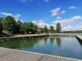Drewniany pomost nad zieloną wodą jeziora Czos, z altaną i drzewami w tle, pod błękitnym niebem z chmurami.