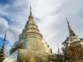 Złote stupy świątyni Wat Phra Singh w Chiang Mai na tle błękitnego nieba z chmurami.