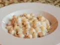 Kluski gnocchi w kremowym sosie z tartą truflą na białym talerzu.