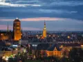 Widok na oświetlone zabytkowe centrum Gdańska o zmierzchu, z dominującą Bazyliką Mariacką i Ratuszem Głównego Miasta.