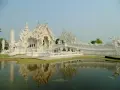 Biała świątynia Wat Rong Khun w Tajlandii z odbiciem w stawie.