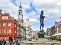 Pomnik króla na Rynku w Poznaniu, w tle kolorowe kamienice i ratusz.
