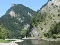Rzeka Dunajec w przełomie, otoczona stromymi, zalesionymi górami i skalnymi zboczami.