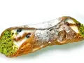 Sycylijski cannolo z kremem, pistacjami i borówkami, posypany cukrem pudrem.