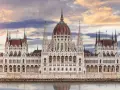 Budynek Parlamentu w Budapeszcie nad Dunajem, z czerwoną kopułą i węgierską flagą, o zachodzie słońca.