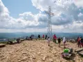 Grupa turystów na szczycie Tarnicy przy metalowym krzyżu, z widokiem na góry.