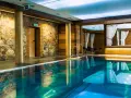 Basen w hotelu SPA z kamienną ścianą i drewnianymi elementami, z zasłonami w tle.