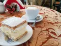 Kremówka posypana cukrem pudrem i filiżanka kawy na stoliku.