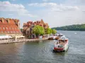 Port w Mikołajkach z zacumowanymi statkami wycieczkowymi i budynkami z czerwonymi dachami. Wspaniałe atrakcje w Mikołajkach czekają na turystów.
