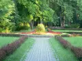 Kamienista ścieżka prowadzi przez park z kwitnącymi rabatami kwiatowymi i zielenią.