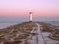 Latarnia morska w kształcie wiatraka na kamiennym falochronie o zachodzie słońca.