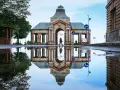 Odbicie zabytkowej budowli z kolumnadą w kałuży po deszczu.