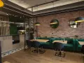 Nowoczesne wnętrze restauracji z ceglaną ścianą, zielonymi kanapami i drewnianymi stołami.