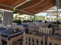 Stoliki w restauracji z niebiesko-białymi obrusami i białymi krzesłami, pod markizą.