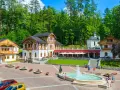 Plac Dietla w Szczawnicy z fontanną, budynkami uzdrowiskowymi i lasem w tle.