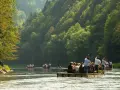 Flisacy na tratwach płyną Dunajcem wśród zielonych wzgórz.