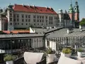 Widok z tarasu na Wawel, z meblami wypoczynkowymi i roślinami w donicach.