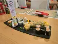 Talerz sushi z różnymi rolkami, w tym smażonymi i z łososiem, na czarnej desce.