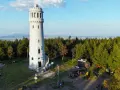 Kamienna wieża widokowa na szczycie góry otoczona lasem, z widokiem na krajobraz.
