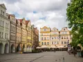 Kolorowe kamienice z arkadami na rynku w Jeleniej Górze, z drzewem w kwiecie po prawej.