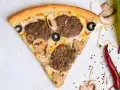 Kawałek pizzy z mięsem mielonym, pieczarkami i oliwkami na jasnym tle.