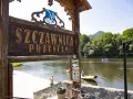 Drewniany szyld "Szczawnica Przystań" nad rzeką z tratwami i górami w tle.
