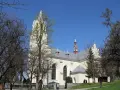 Jasny kościół św. Wojciecha w Szczawnicy z wieżą, otoczony drzewami.