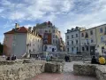 Ruiny zamku w Lublinie z ludźmi odpoczywającymi na kamiennych murach i zabytkowymi kamienicami w tle.