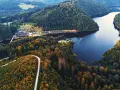 Widok z lotu ptaka na jezioro Bystrzyckie otoczone lasami, z krętą drogą i zabudowaniami.