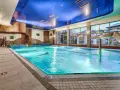 Basen hotelowy z niebieskim sufitem i dużymi oknami, woda w basenie jest turkusowa.
