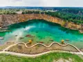 Turkusowe jezioro w kamieniołomie z drewnianą kładką i altaną.