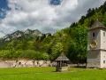 Ruiny klasztoru z wieżą i studnią na tle zielonych gór i chmur.