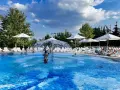 Rodzinna zabawa w hotelu z basenem na Mazurach. Dzieci pluskają się w wodzie, dorośli odpoczywają na leżakach pod białymi parasolami.