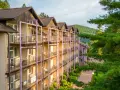 Hotel z balkonami w otoczeniu zieleni i gór.
