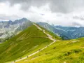 Szlak górski z turystami na tle skalistych szczytów i zielonych zboczy.