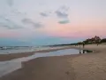 Plaża w Łebie o zachodzie słońca z widokiem na morze i budynek z czerwonym dachem.