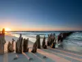 Zachód słońca nad morzem, drewniane pale na plaży tworzą romantyczny nastrój. Fajne miejsce nad morzem dla dwojga.