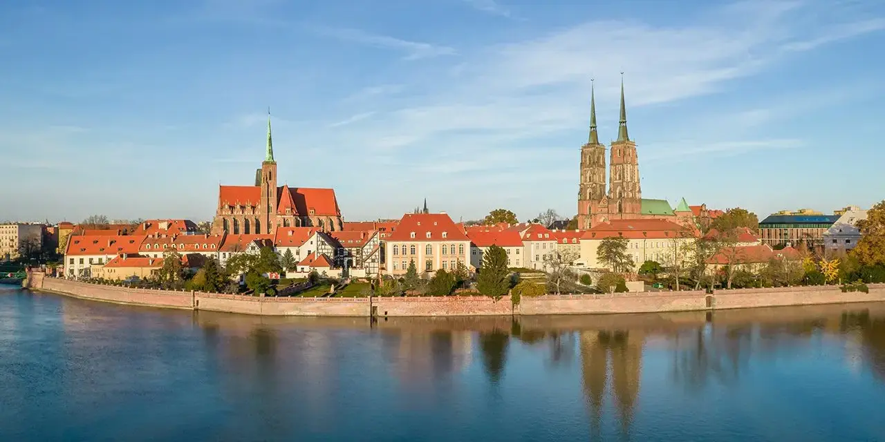 Widok na Ostrów Tumski we Wrocławiu z rzeką i odbiciem budynków w wodzie.
