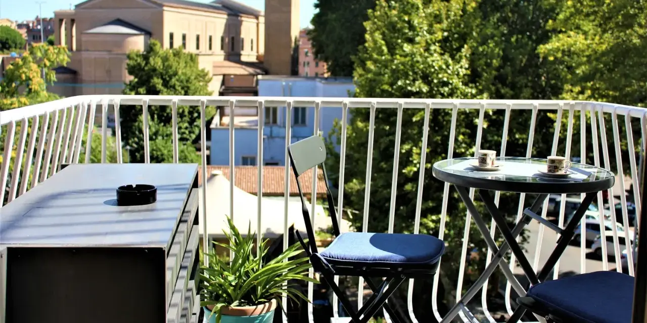 Balkon z widokiem na rzymskie budynki i zieleń, stolik z kawą.