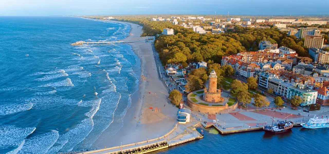 Widok z lotu ptaka na plażę, morze, latarnię morską i zabudowania Kołobrzegu.