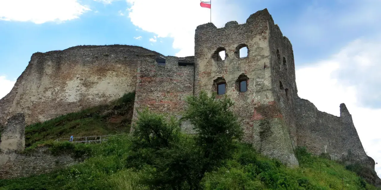 Ruiny zamku w Czorsztynie na wzgórzu, z polską flagą na wieży.