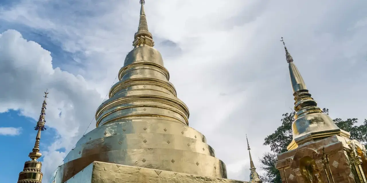 Złote stupy świątyni Wat Phra Singh w Chiang Mai na tle błękitnego nieba z chmurami.