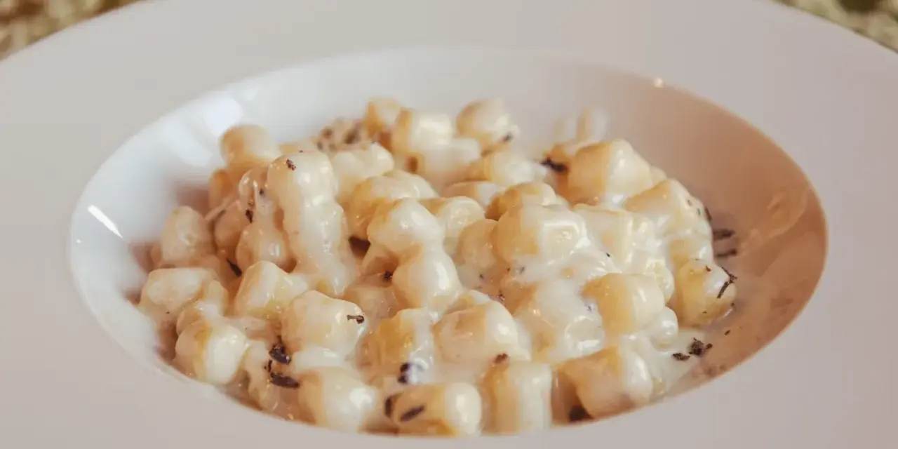 Kluski gnocchi w kremowym sosie z tartą truflą na białym talerzu.