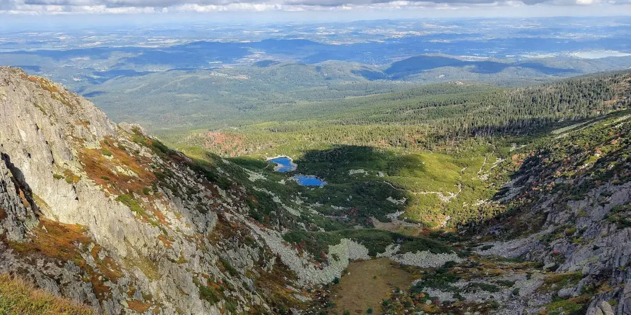 Widok z góry na skaliste zbocze, dolinę z dwoma stawami i lasy w tle.