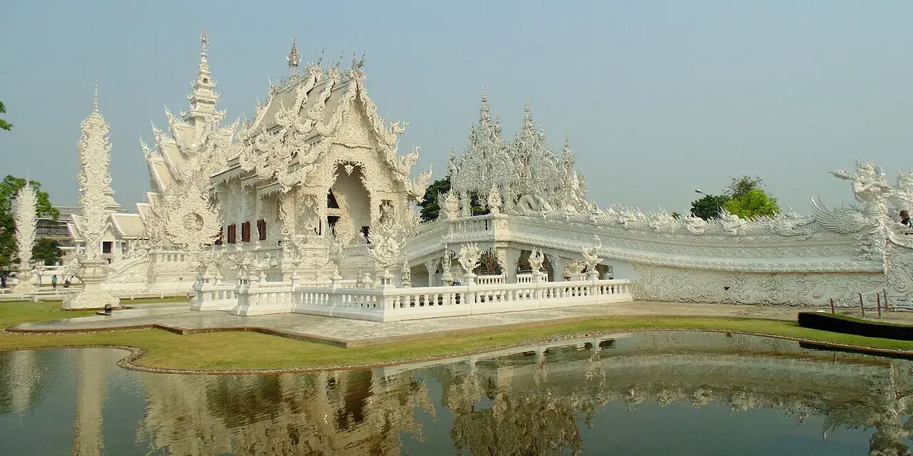 Biała świątynia Wat Rong Khun w Tajlandii z odbiciem w stawie.